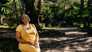 Lady sitting on a bench enjoying the sunshine with eyes closed.