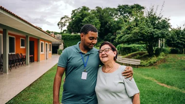 Man with his arm around the shoulder of an older lady while walking outside