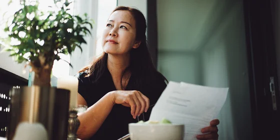 Middle aged lady holding documents while staring wistfully out a window